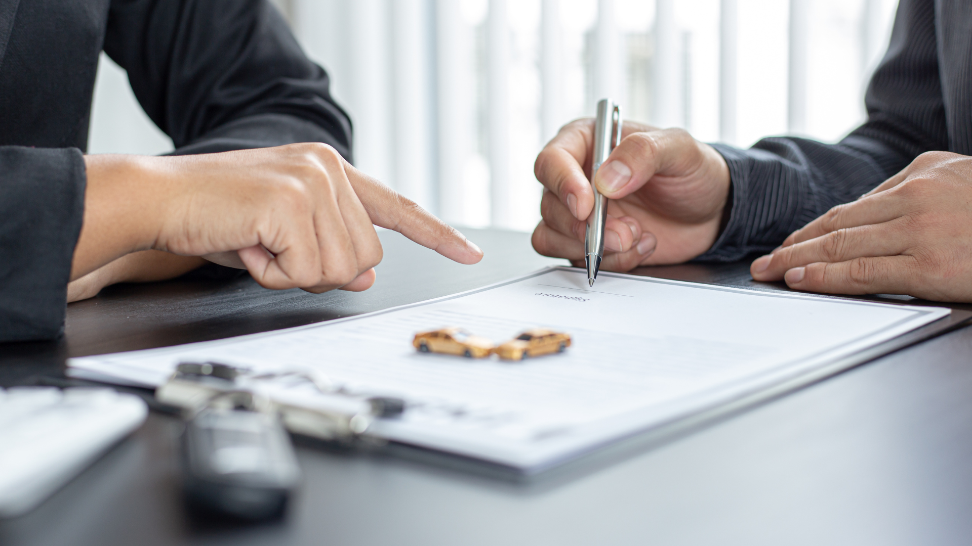 Two people pointing and writing on a document at a desk with a calculator and keys nearby