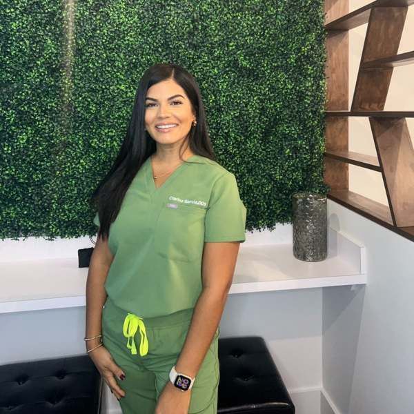 A female dentist wearing a white coat and a black scrub is smiling for the camera.