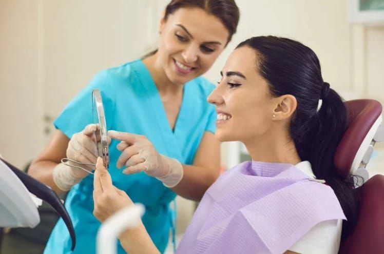 A woman is sitting in a dental chair while a dentist examines her teeth.