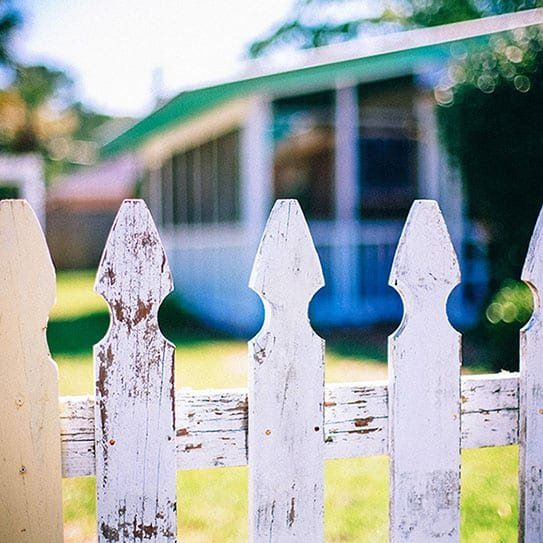 A white picket fence with a house in the background