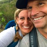Smiling couple taking a close-up selfie outdoors with green hills in the background