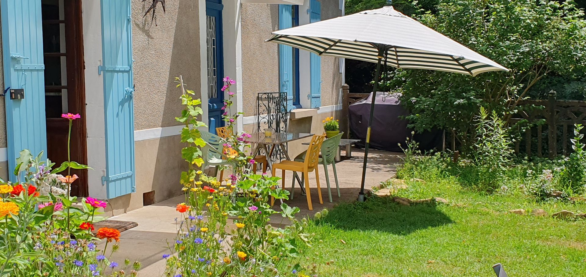 Une maison avec des volets bleus et un parasol devant