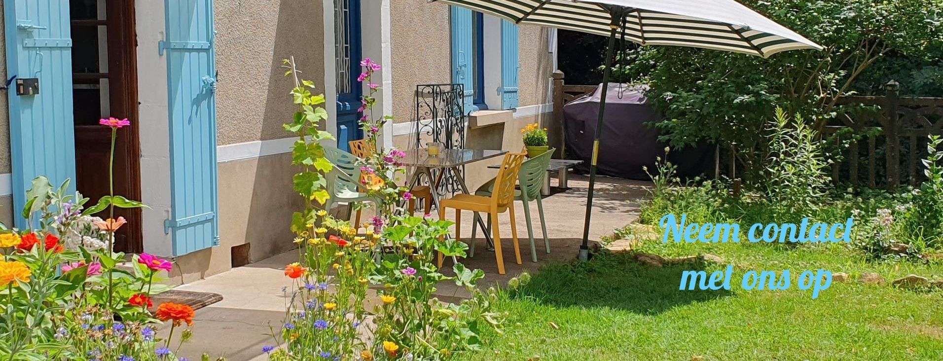 Charmante huisgevel met blauwe luiken, een terras en een kleurrijke tuin.