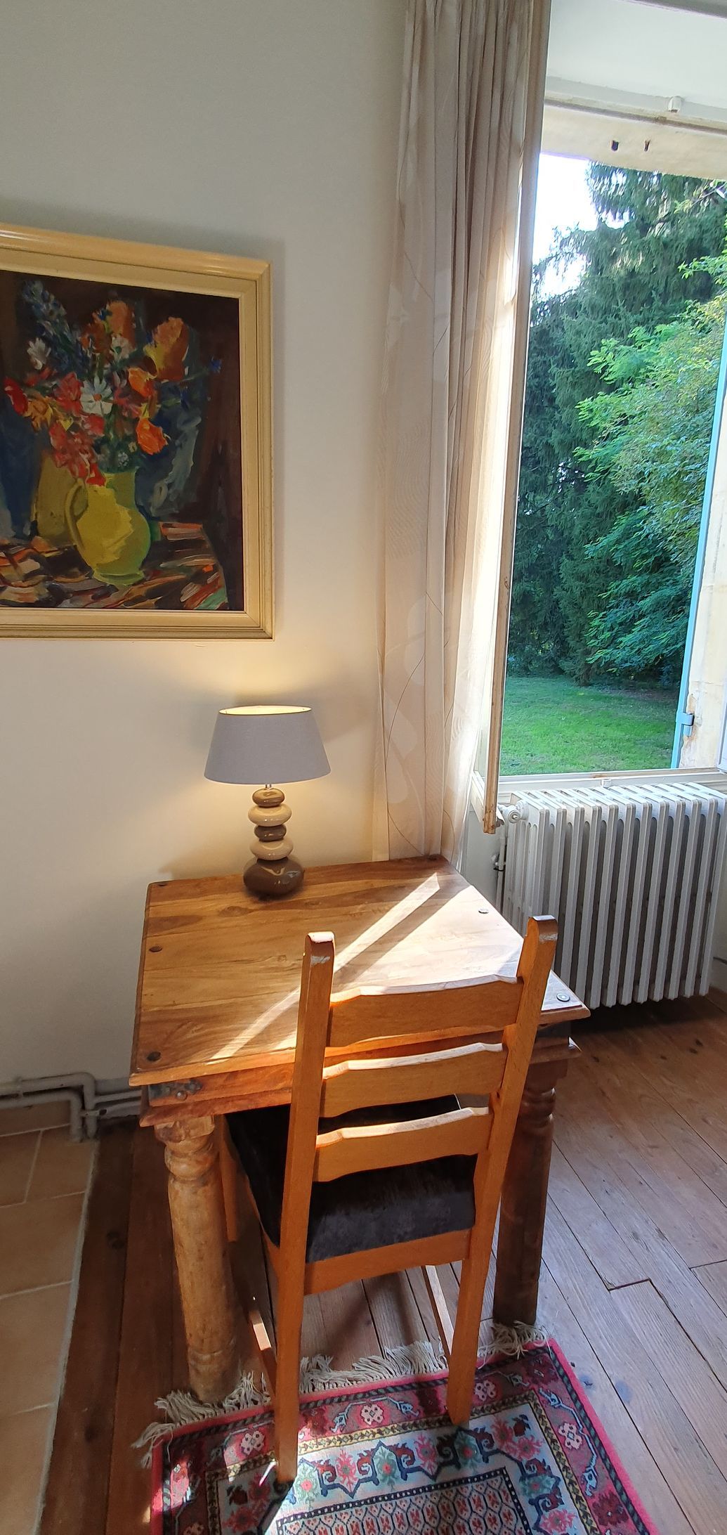 Rays of sunchine on a wooden desk with a lamp and a painting on the wall above it