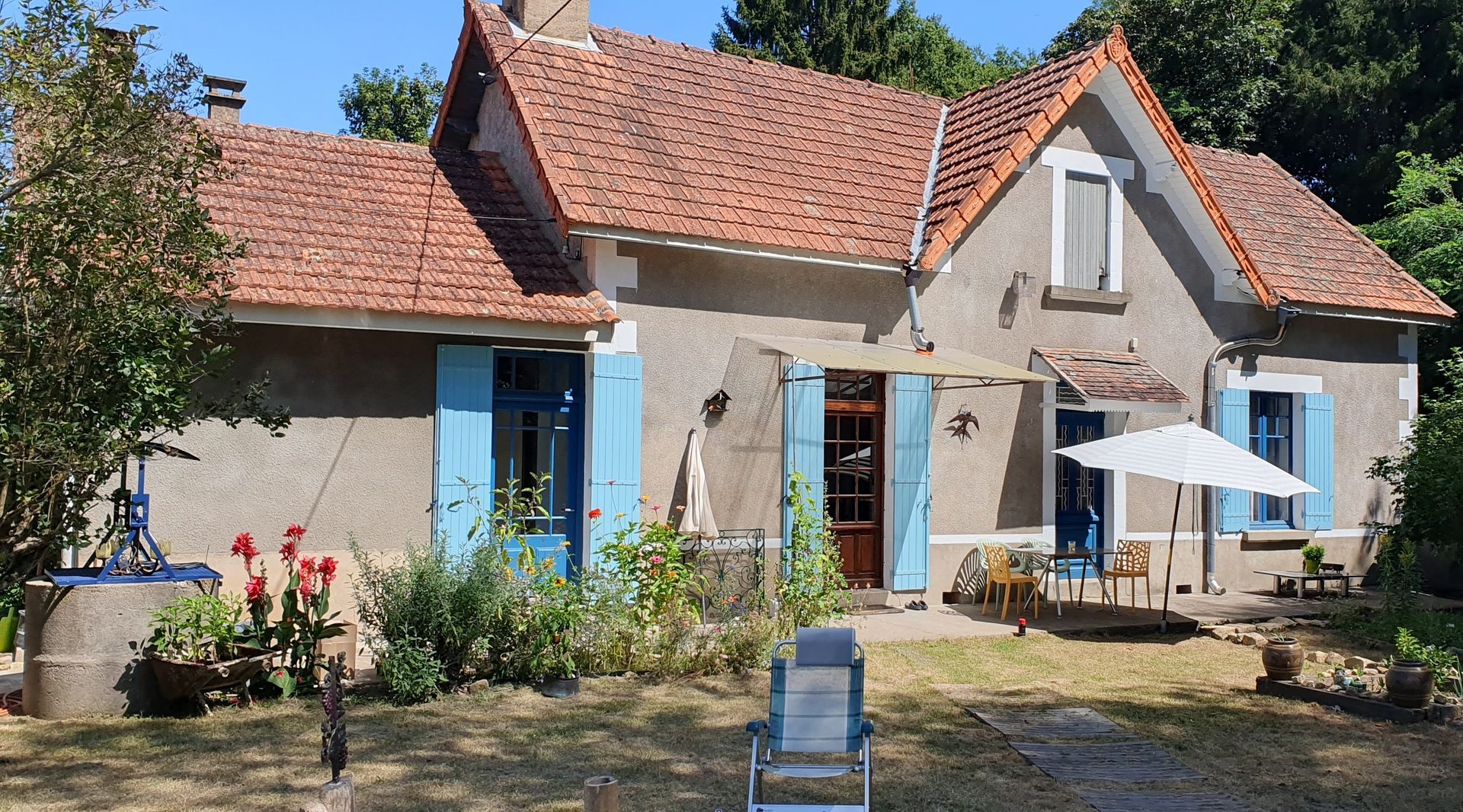 Une maison avec un puit et des volets bleus et un parasol devant