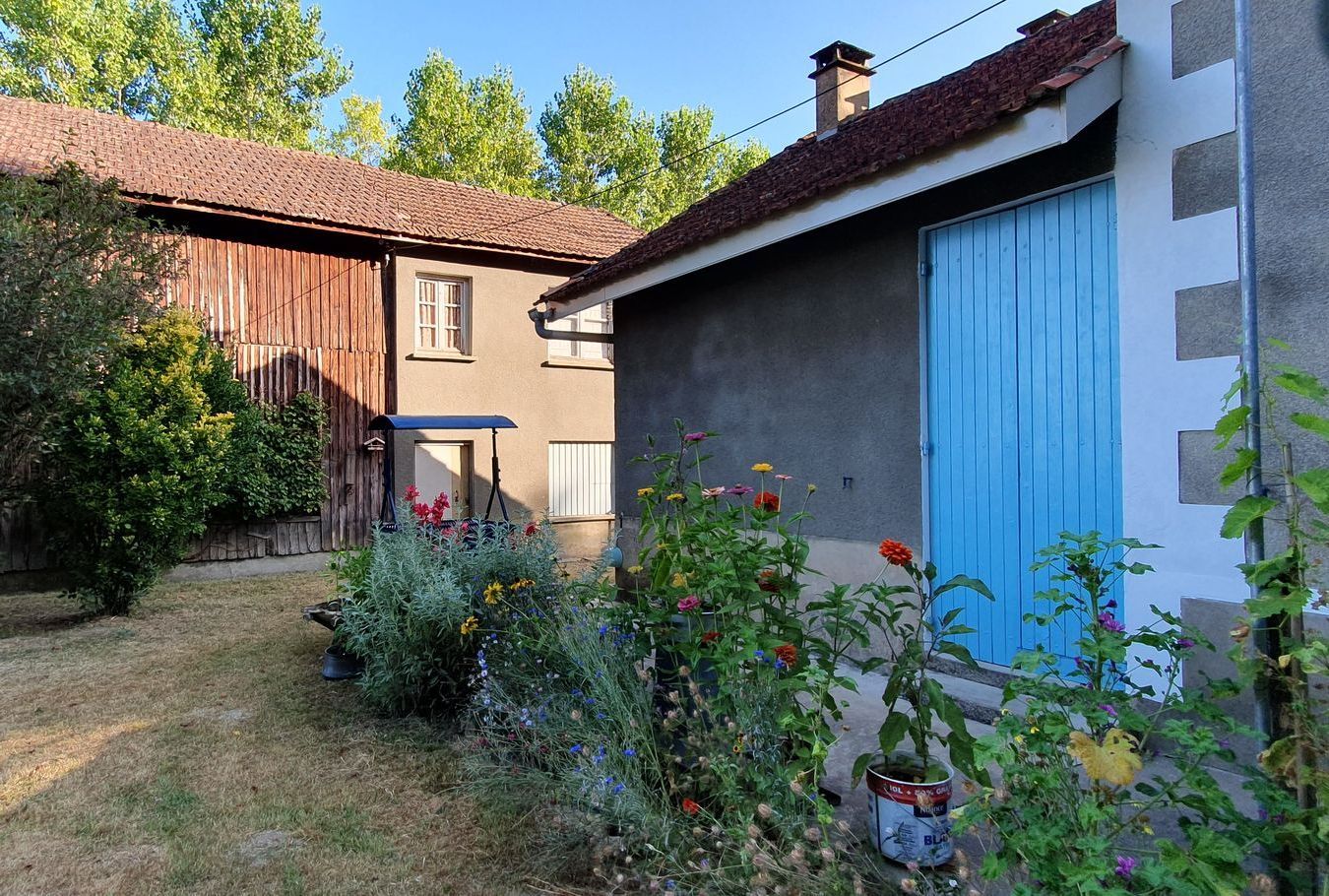 Une grange et une maison avec une porte de garage bleue et des fleurs devant
