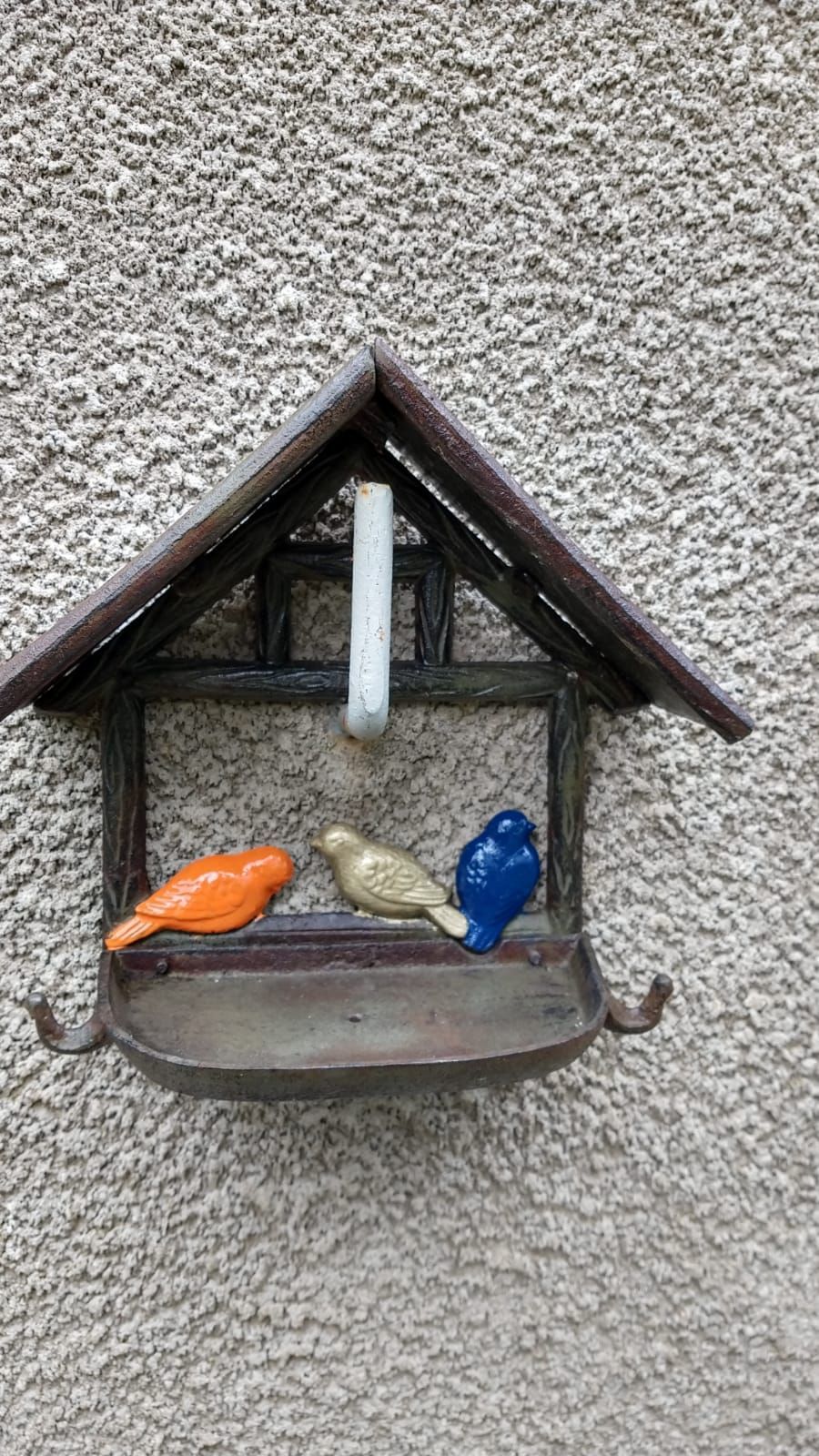Mangeoire à oiseaux avec trois oiseaux à l'intérieur est accrochée à un mur.