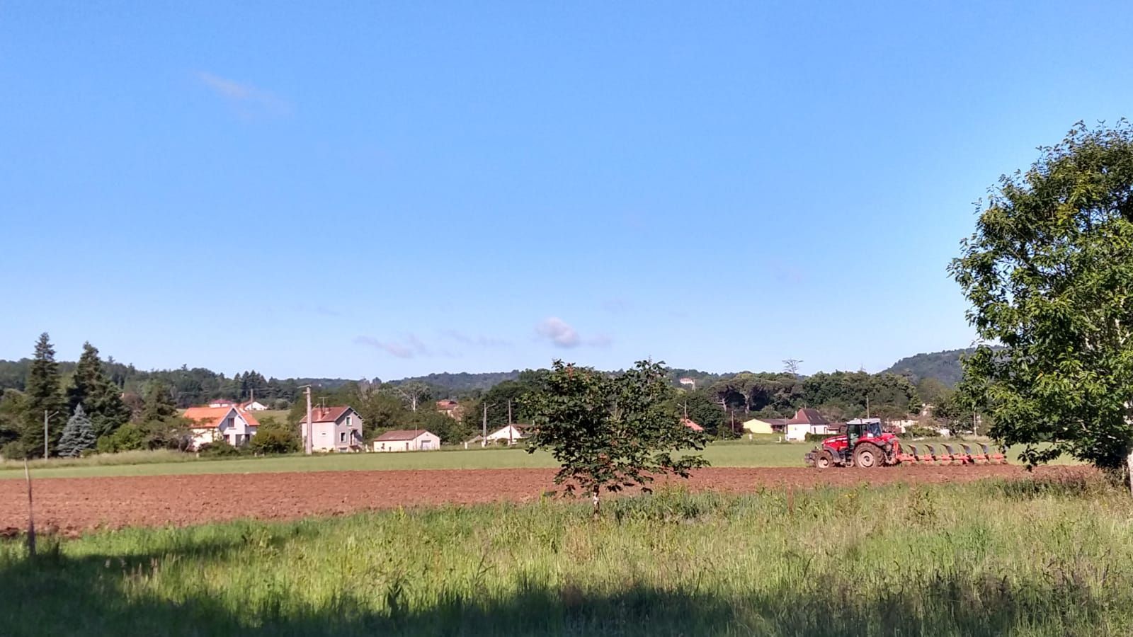 Un tracteur laboure un champ avec des maisons en arrière-plan