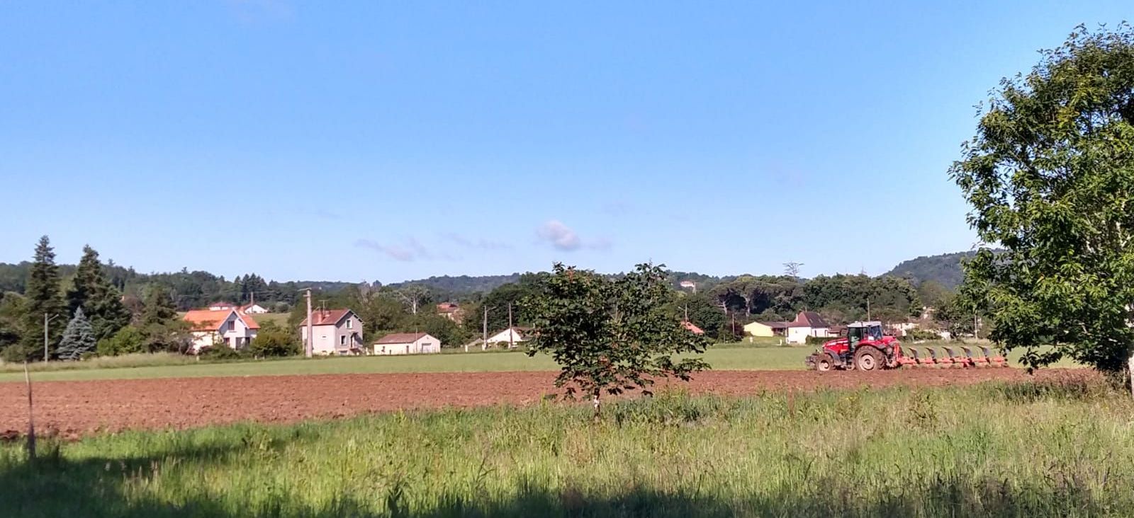 A tractor is plowing a field with houses in the background