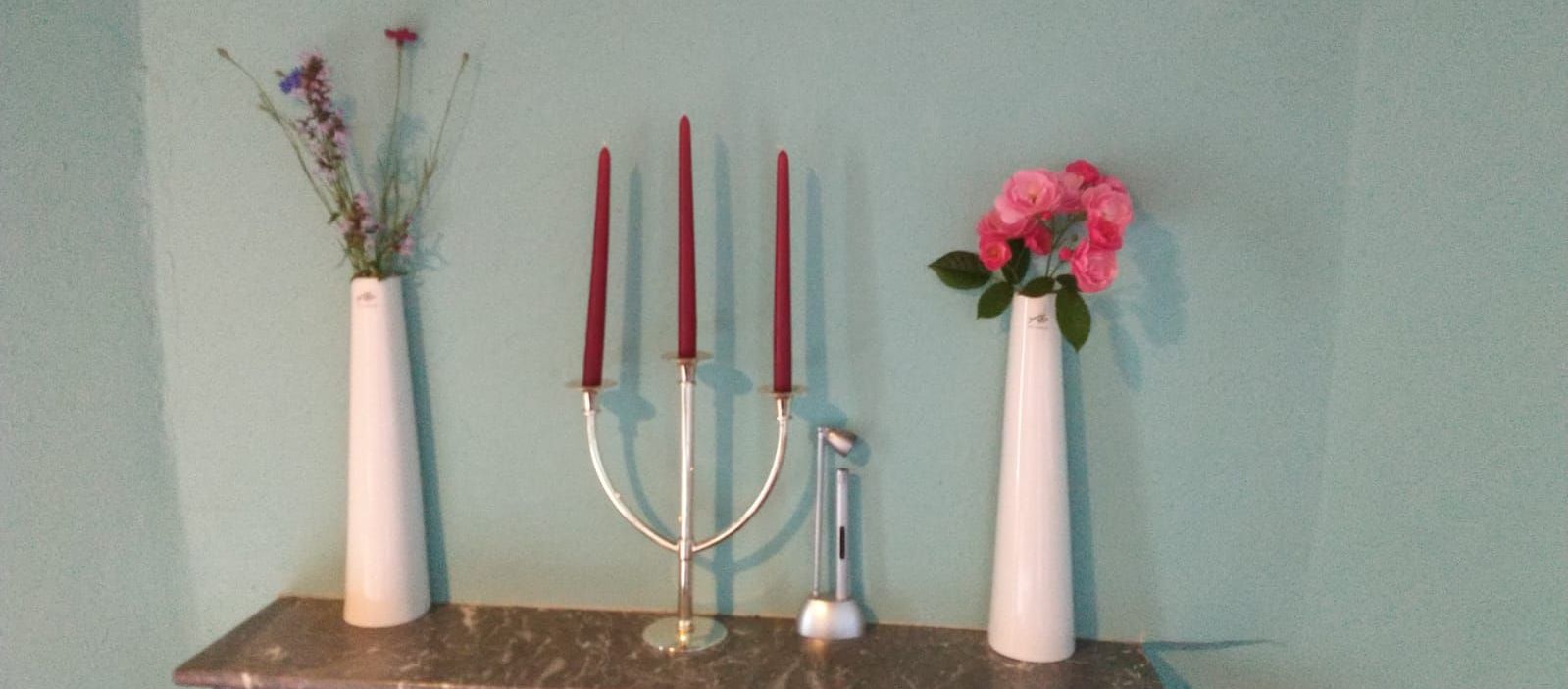 Vazen met bloemen, een kandelaar met kaarsen en een staafmixer op een marmeren blad tegen een turquoise muur.
