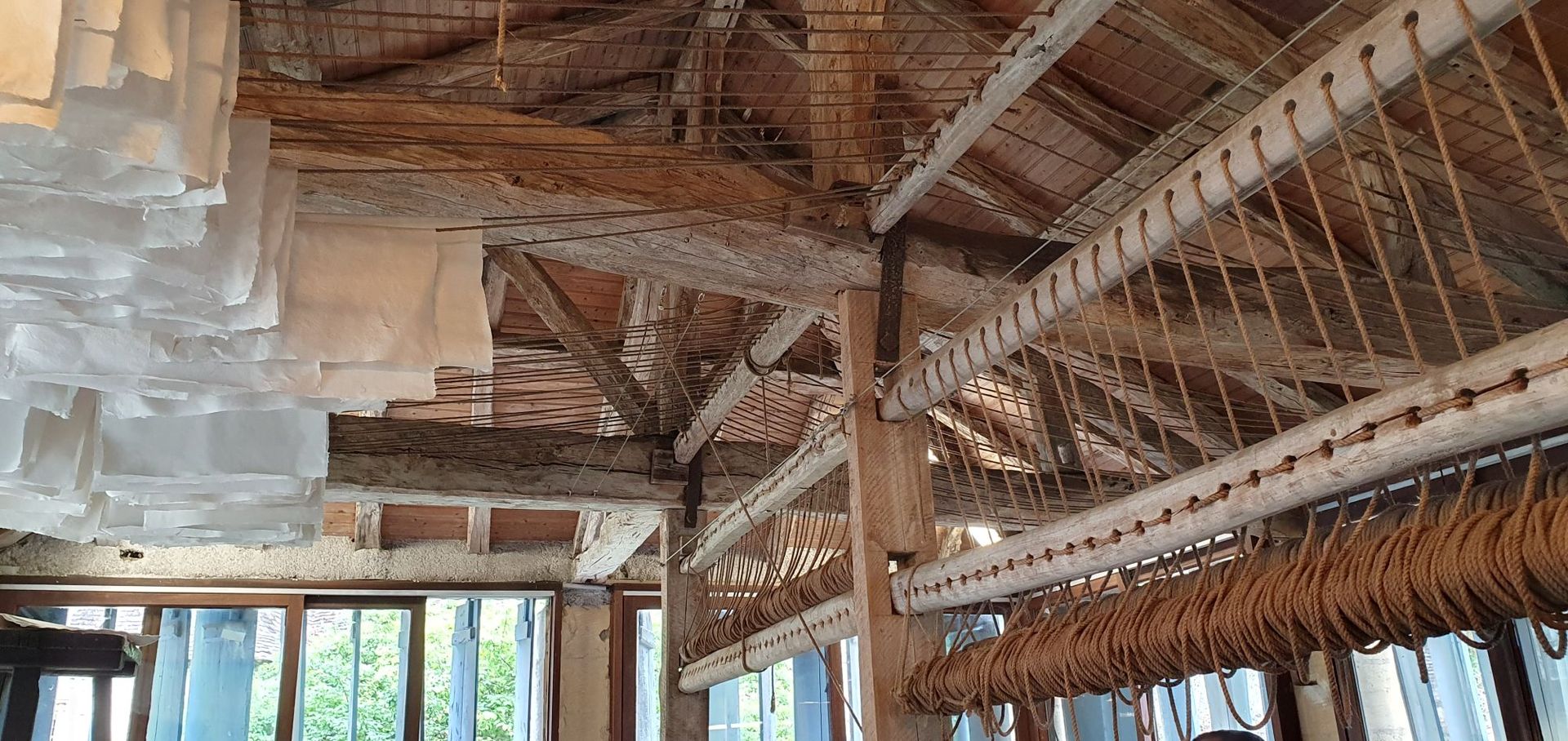 Interieur van een rustiek gebouw met houten balken en een rieten dak. Aan het plafond hangen lampen.