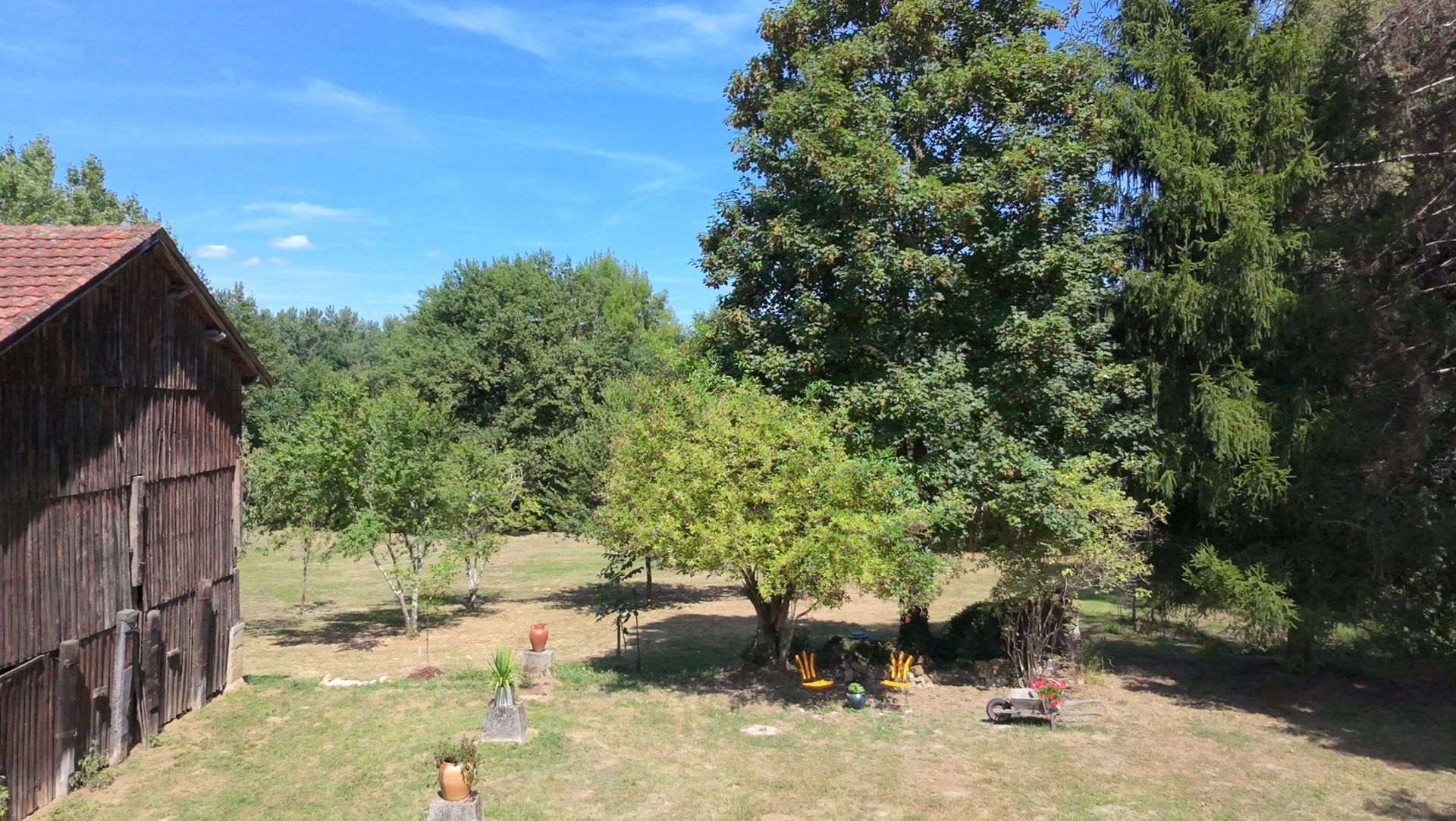 Een houten schuur naast een grasveld met bomen, onder een blauwe hemel.
