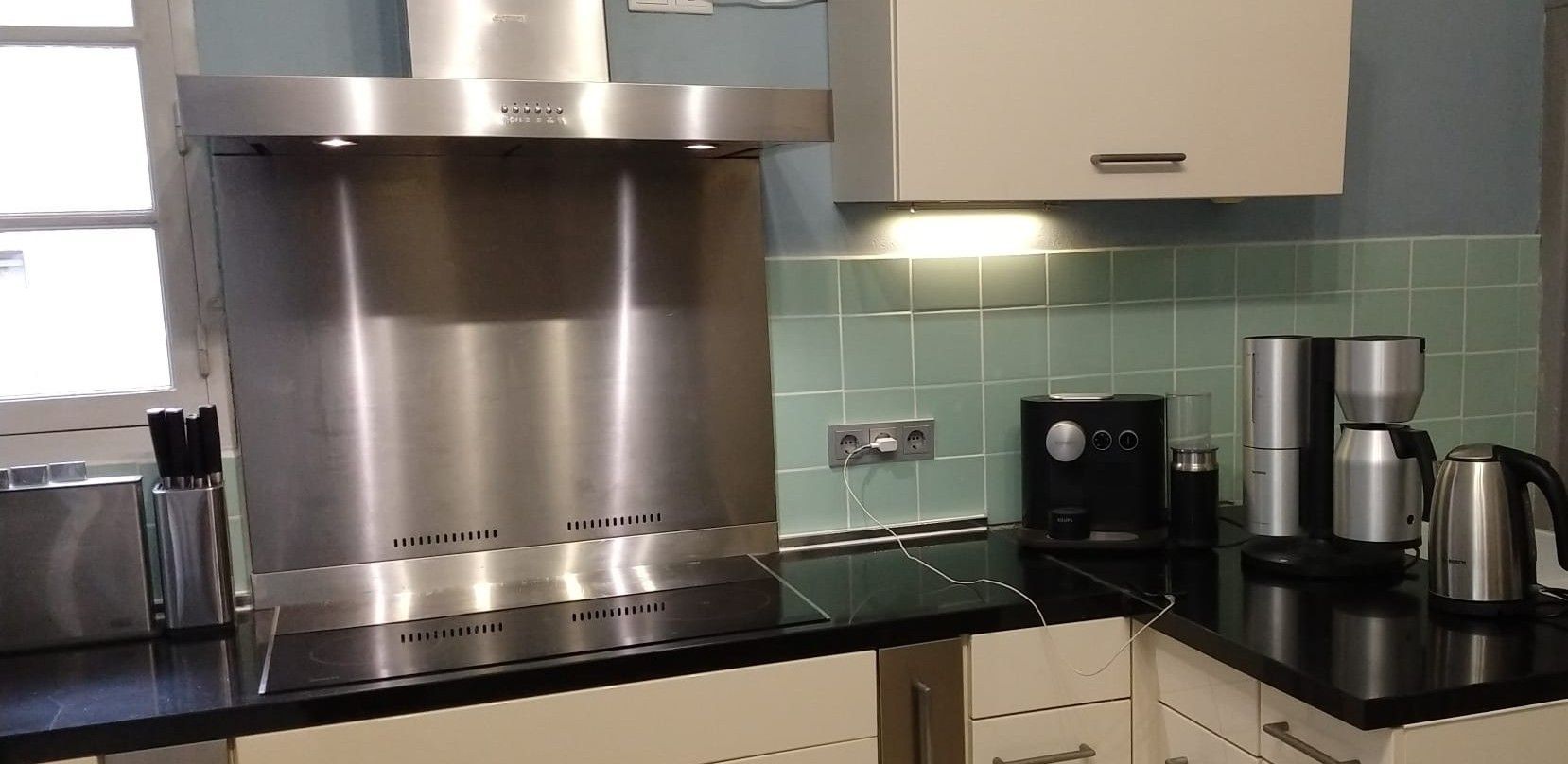 Keukenblad met roestvrijstalen afzuigkap en apparatuur, waaronder een koffiezetapparaat en een waterkoker.