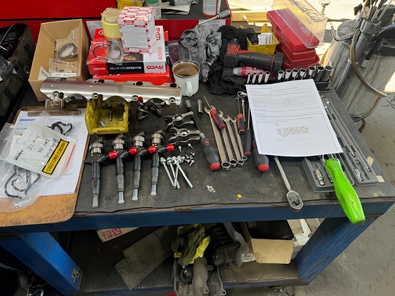 Fuel injectors, spanners, and vehicle parts laid out on a workshop bench at a Nowra mechanic