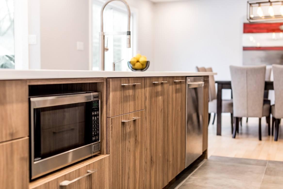 Îlot de cuisine moderne avec armoires en bois, micro-ondes intégré et lave-vaisselle en acier inoxydable.