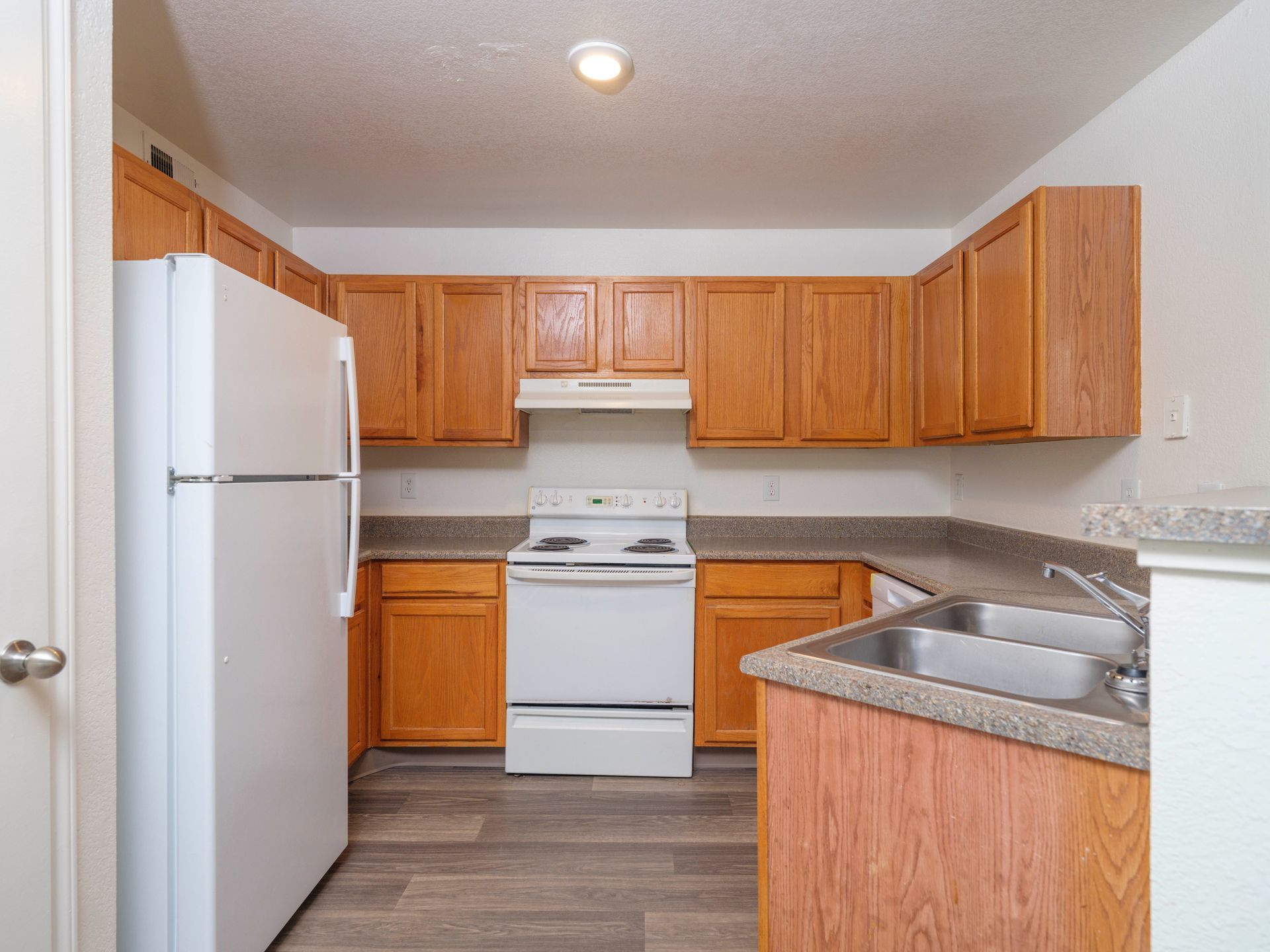 Compact kitchen with wooden cabinets, white appliances, and a gray countertop with double sink