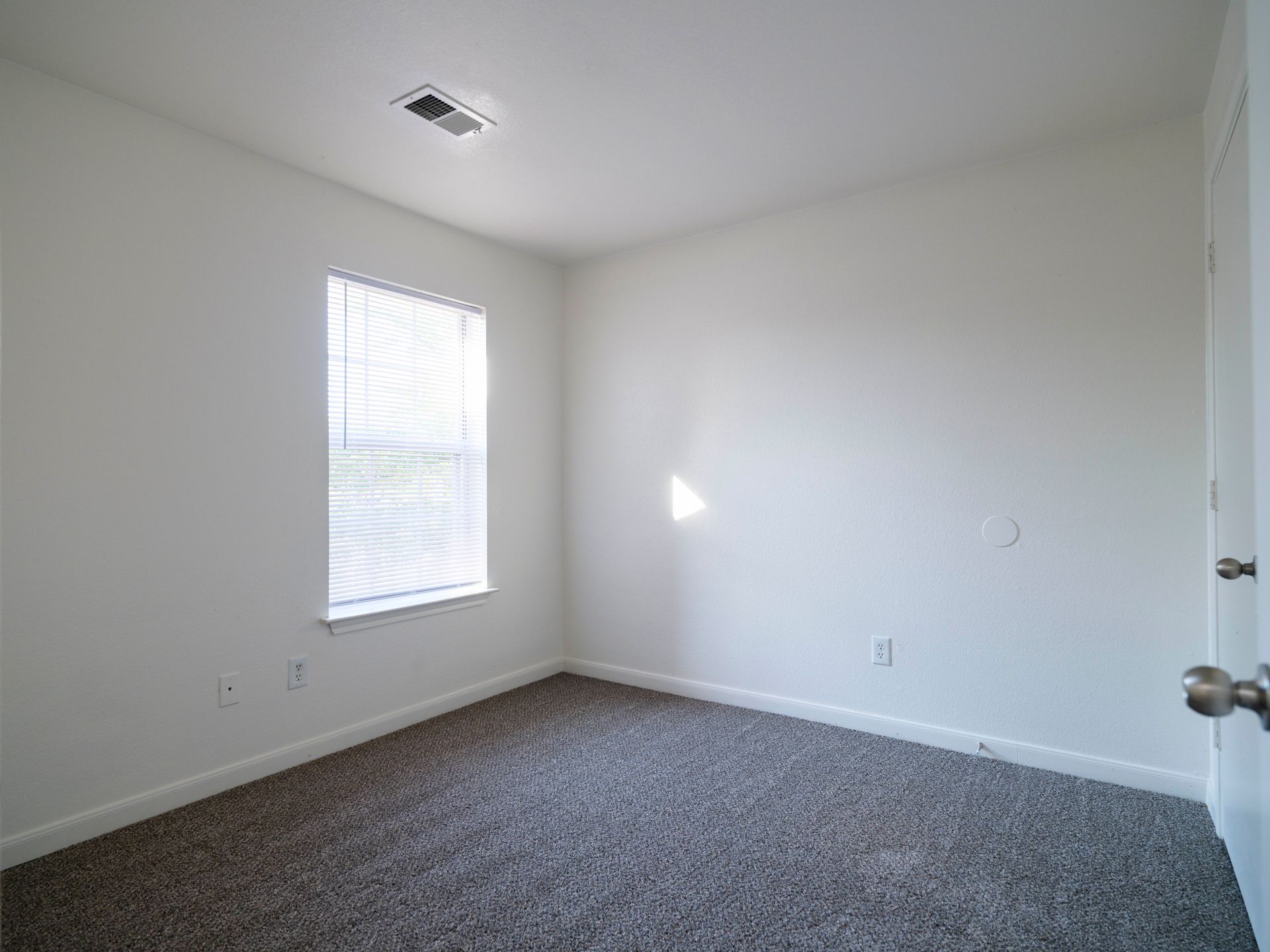 Empty carpeted bedroom with white walls and a window