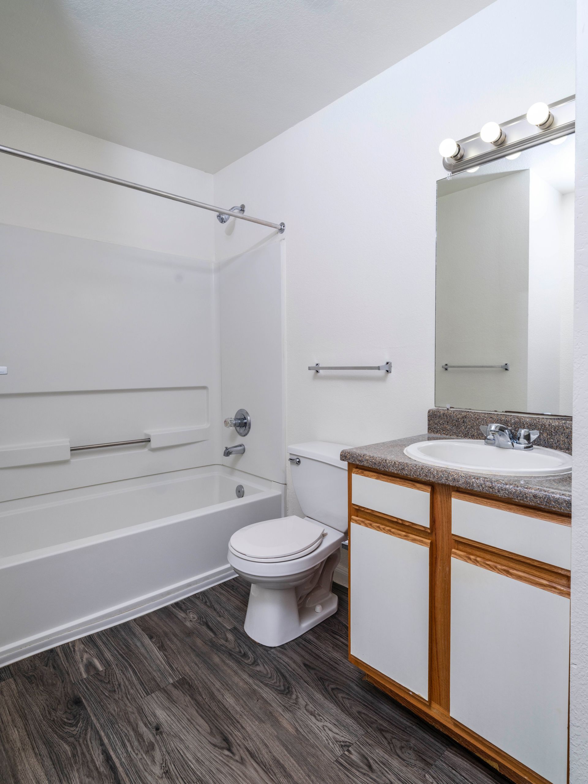 Bathroom with white tub, toilet, and vanity with mirror and lights.