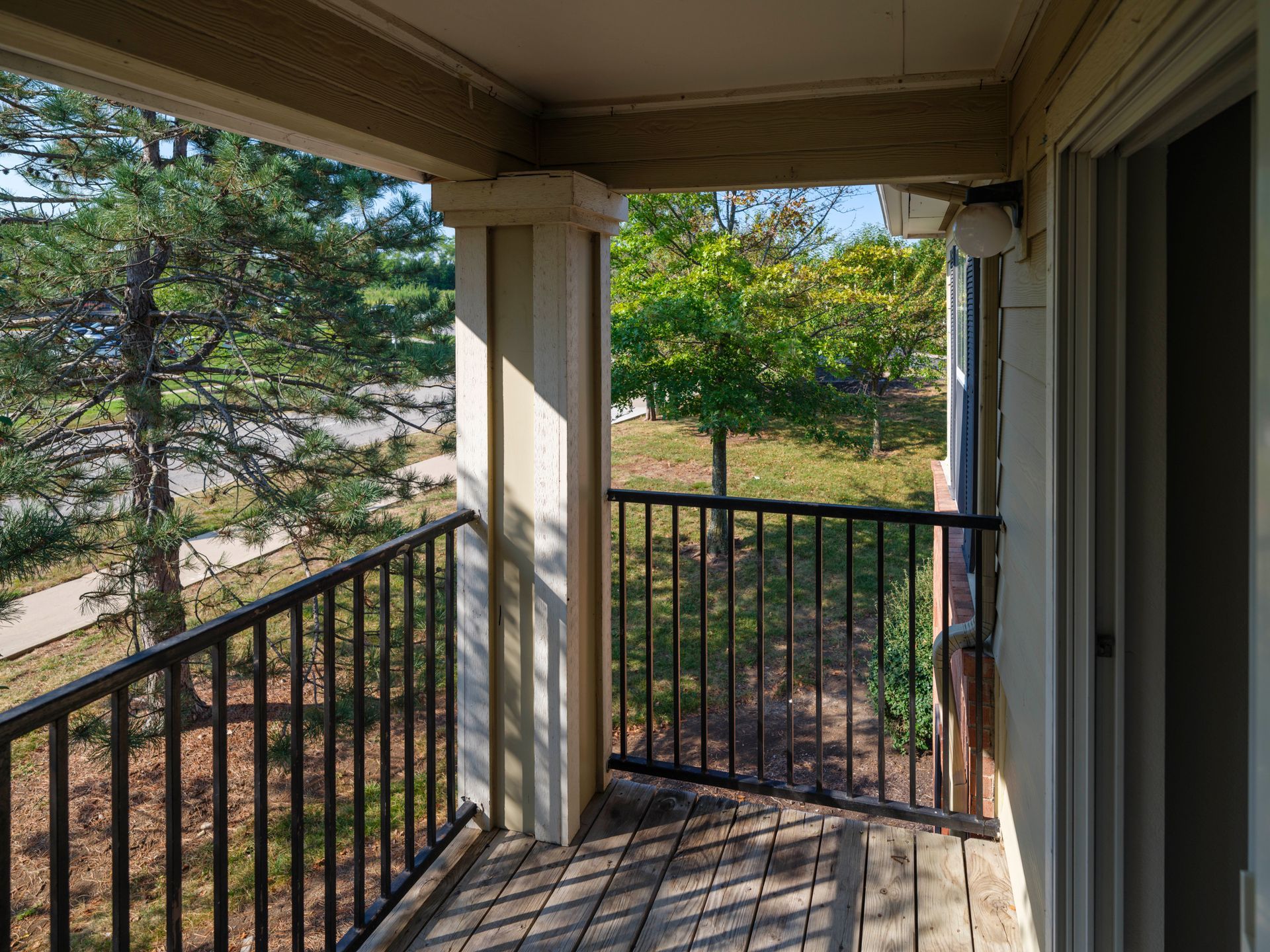 Covered porch with black railing overlooking trees and a sunlit yard