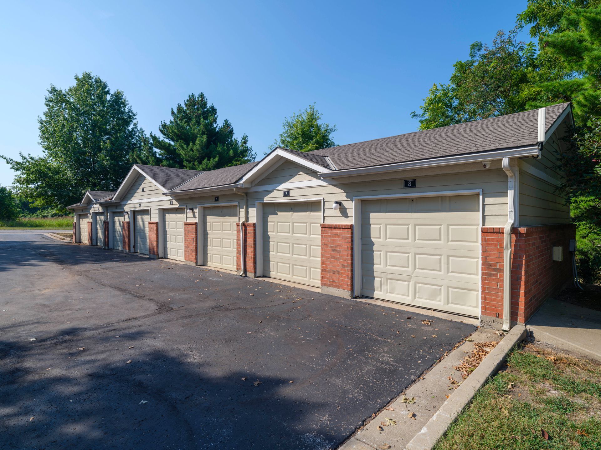 Row of beige garage units with white doors along a paved lot under a clear blue sky