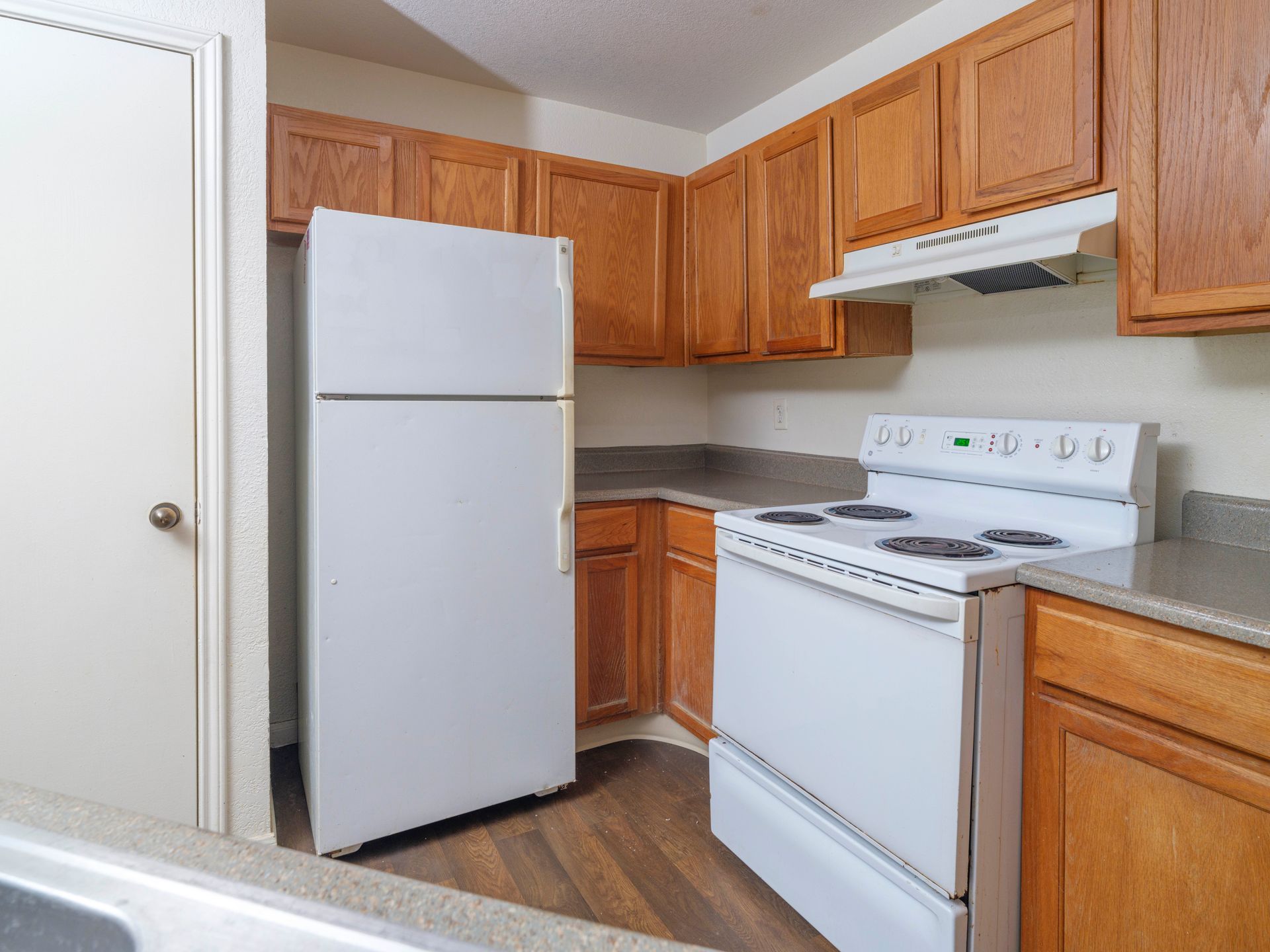 Small kitchen with white appliances, wood cabinets, and wood flooring.
