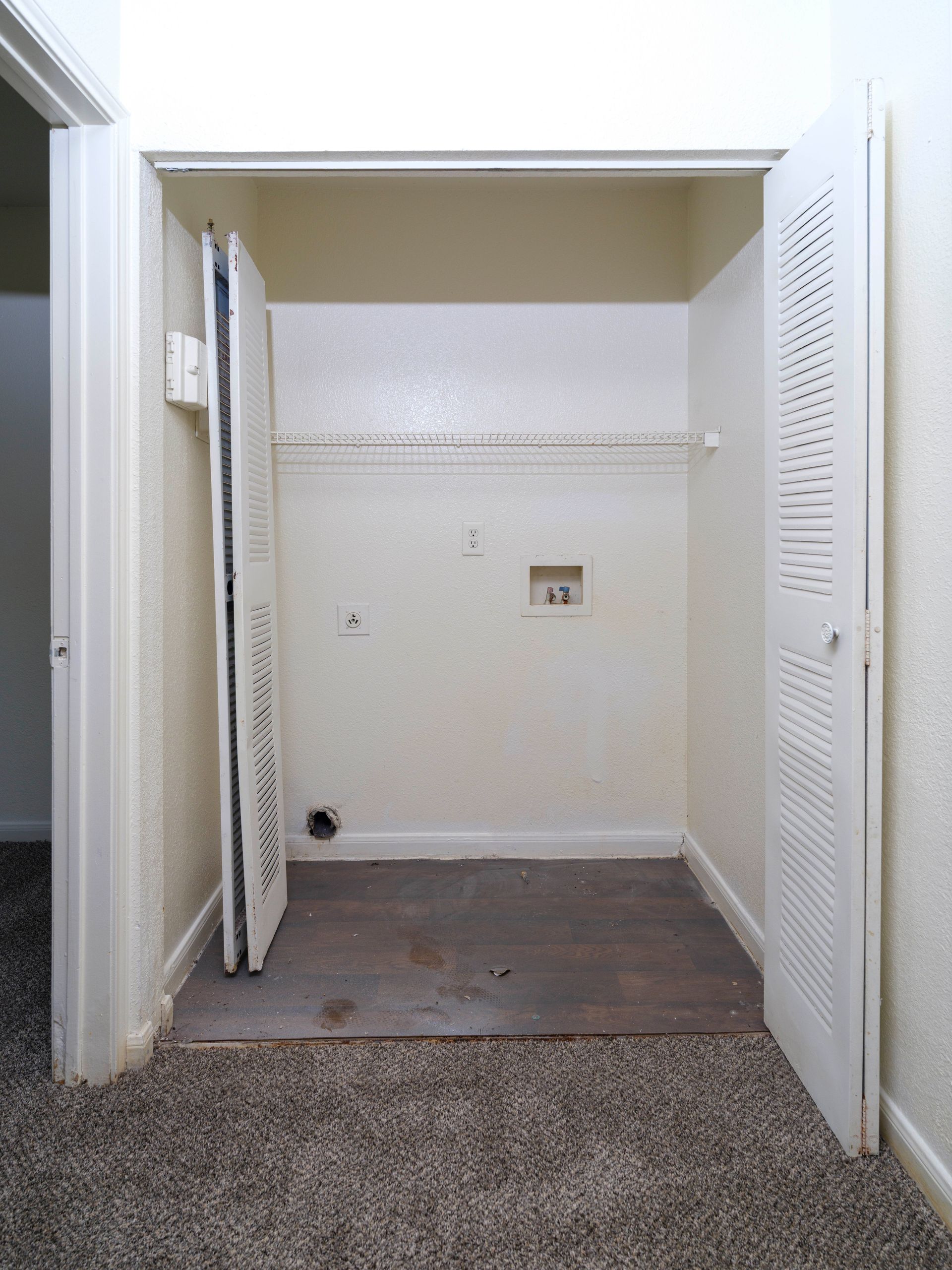 Empty closet alcove with white walls, louvered doors, and carpeted floor