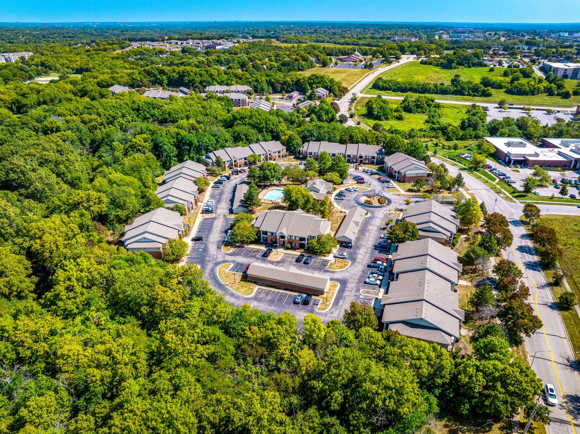 Aerial view of a green residential complex with townhouses, roads, and surrounding trees