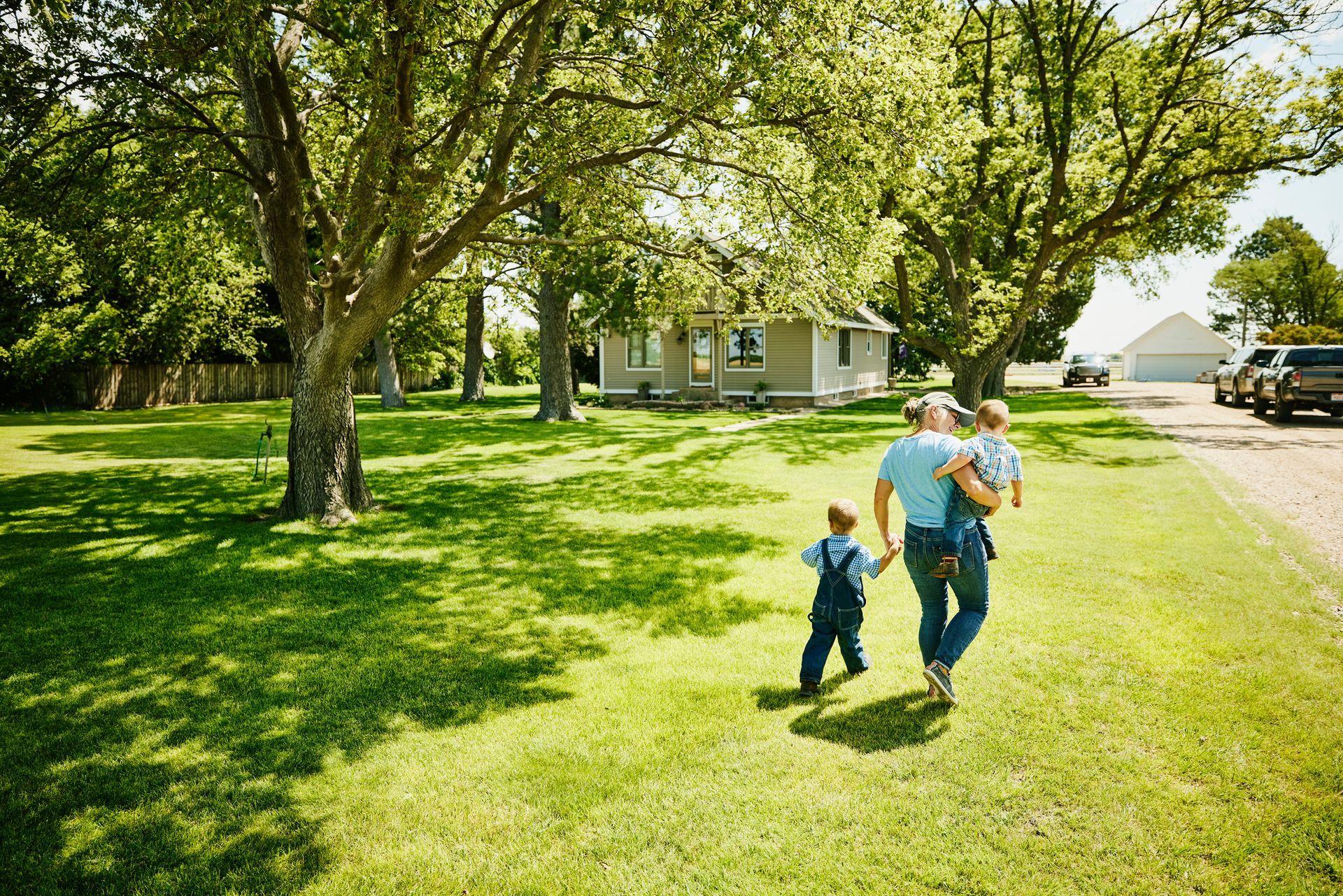 Man walking with two children toward a house with a green lawn.