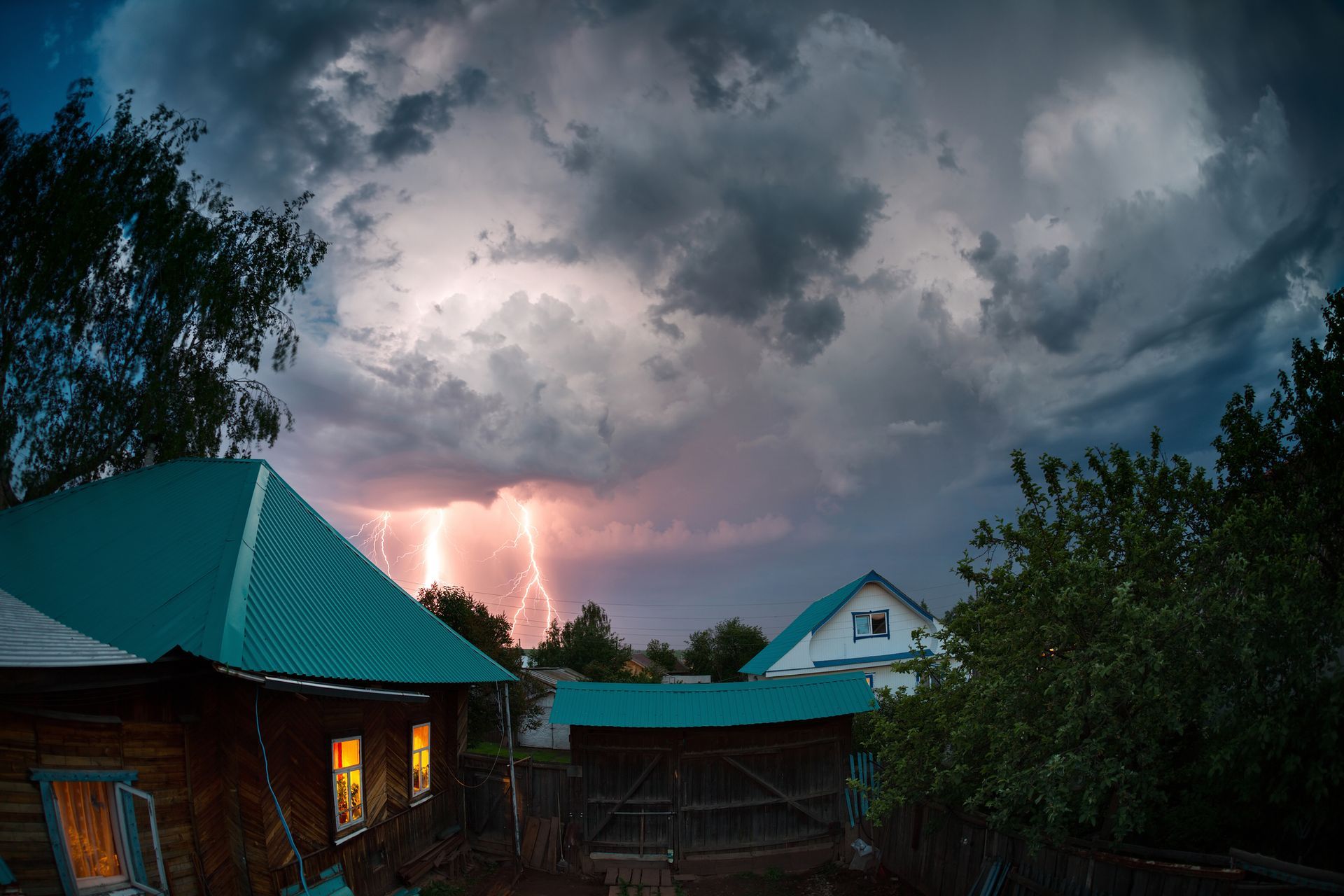 Lightning strikes over a small village with wooden houses, dark stormy sky.