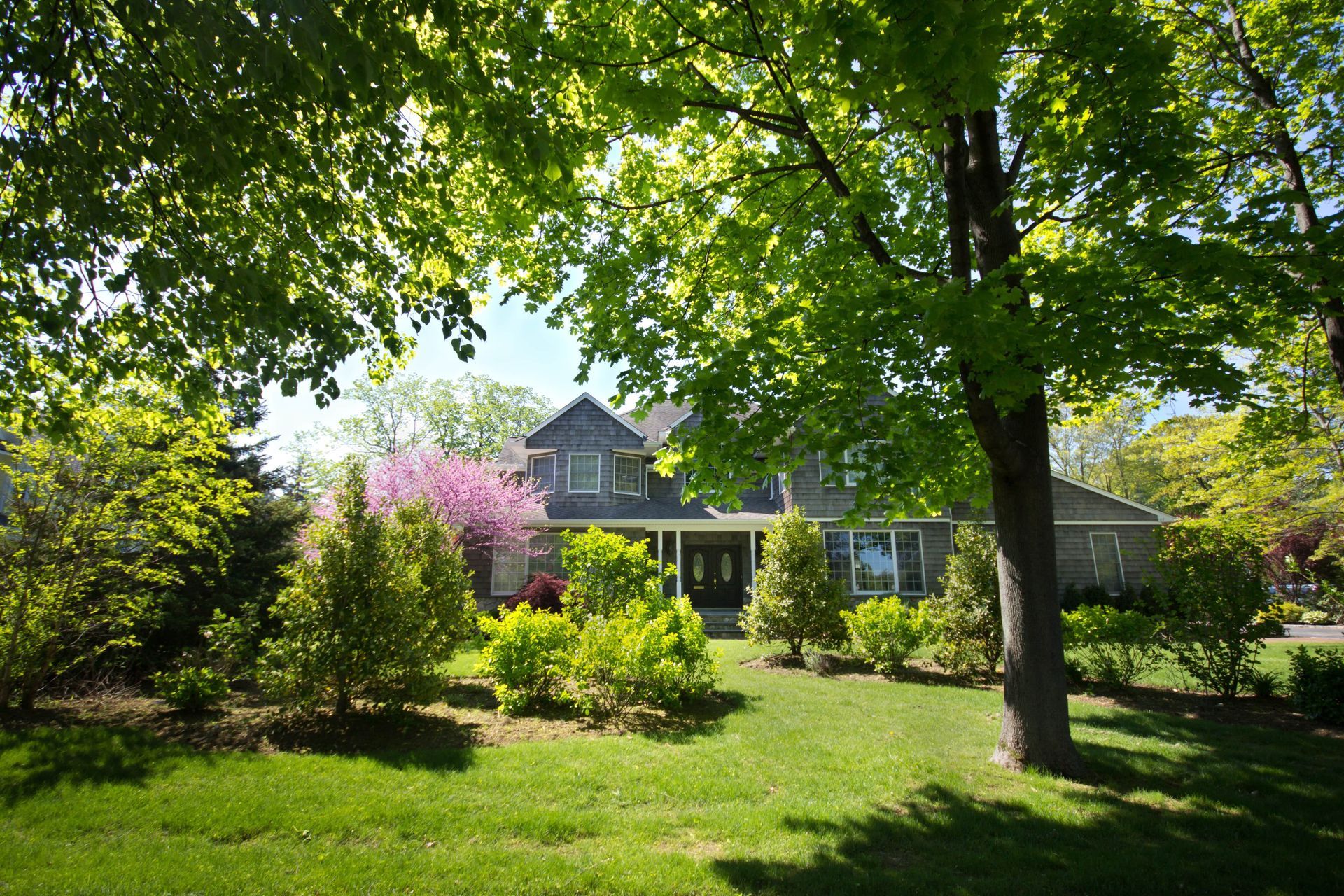 House exterior with green lawn, trees, shrubs, and a clear sky.