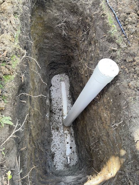Open trench with a white PVC pipe and gravel bed in the ground