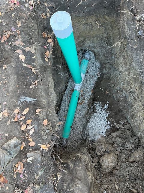 Turquoise pipe emerging from a narrow trench in the dirt, capped with a white top.