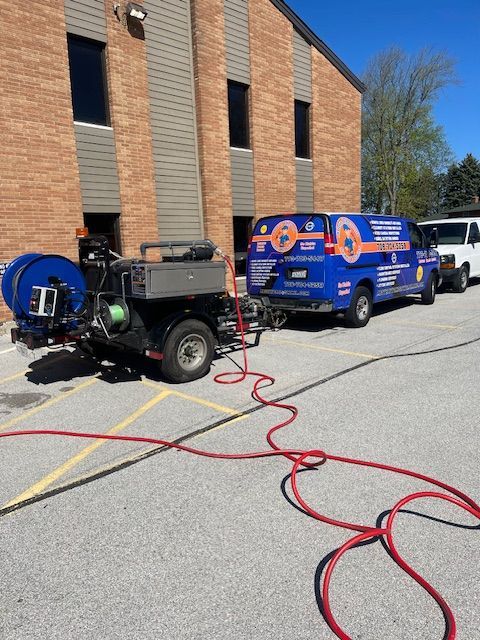 Utility trucks with hoses on pavement beside a brick building, likely sewer or vacuum work
