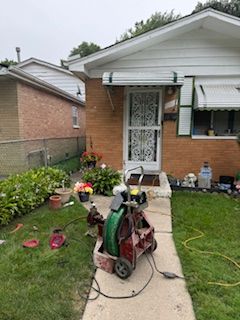Front yard with lawn equipment, flowers, and a house entrance with a white security door
