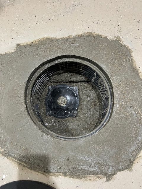 Concrete floor drain with a black circular cap in a gray patch of cement