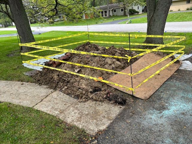 Curbside yard debris pile wrapped in yellow caution tape beside sidewalk and road