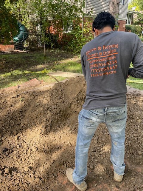Worker in gray shirt and jeans spreads dirt in a backyard landscaping area.