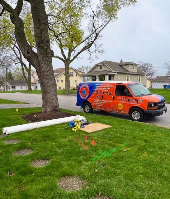 Orange utility van parked on a lawn beside a fallen white pole and a large tree in a suburban yard