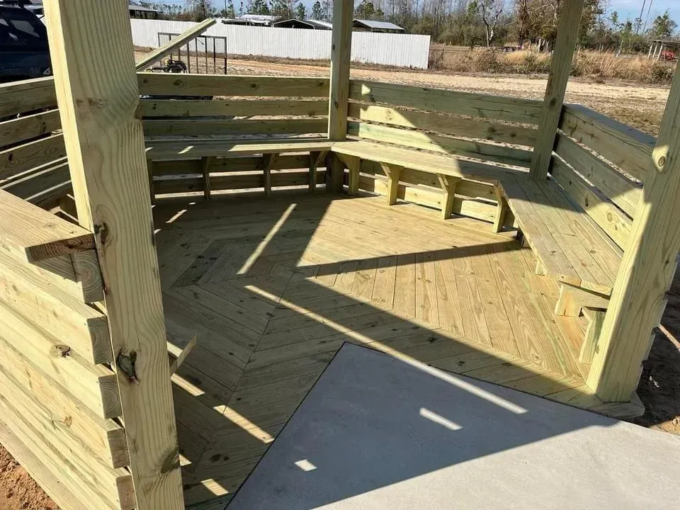 Wooden livestock pen with curved rails and concrete floor in a sunny outdoor area