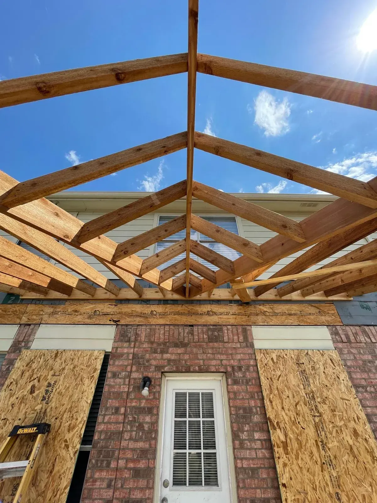 Partially built house roof framing above a brick wall and white door under a blue sky