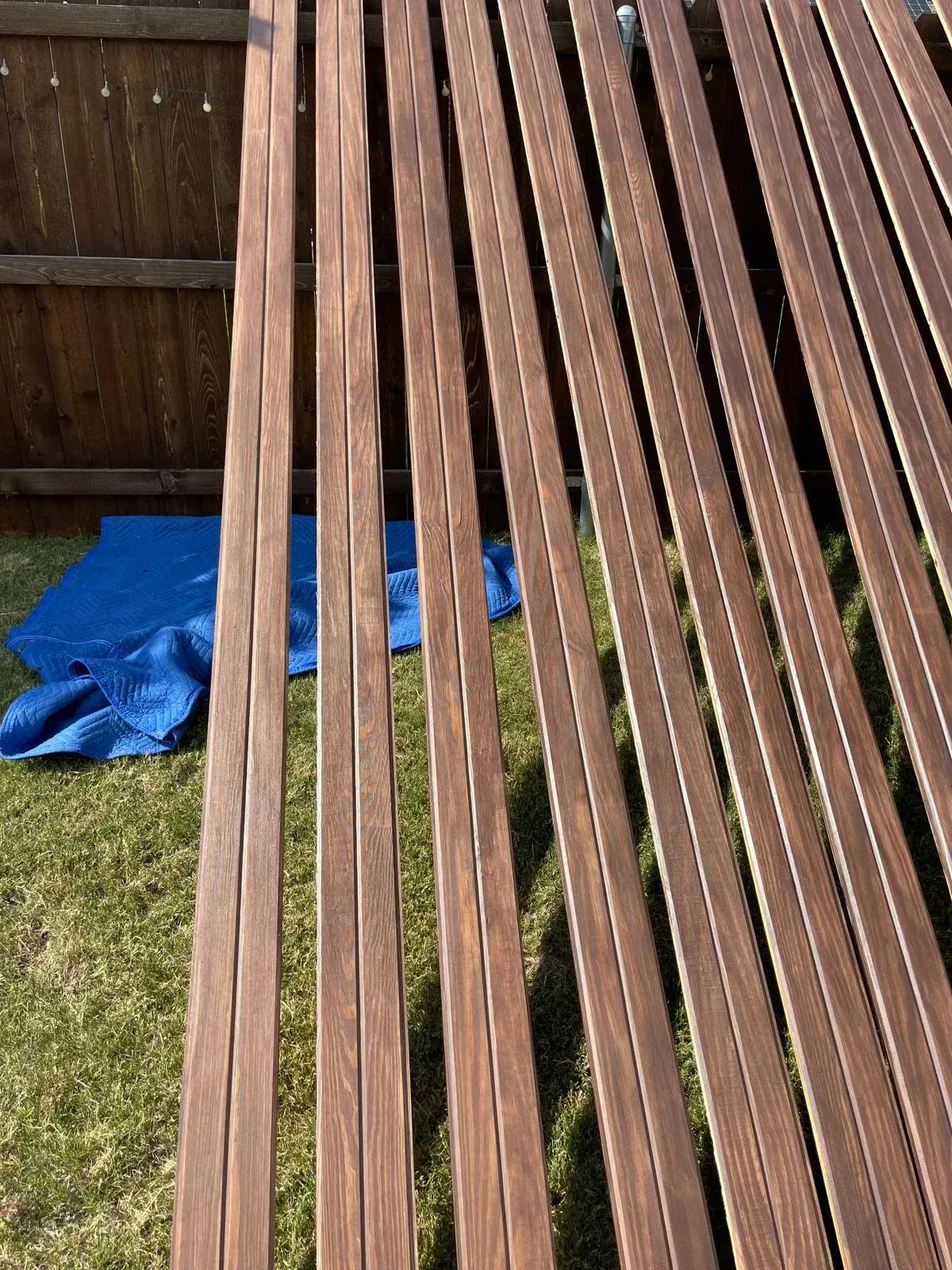 Wooden fence slats leaning over a grassy yard with a blue tarp on the ground