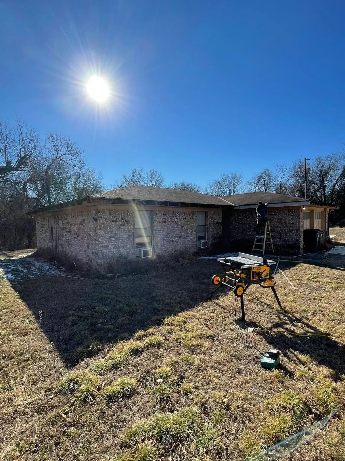 Single-story brick house with a bright sun, yard, and a metal grill in the foreground.