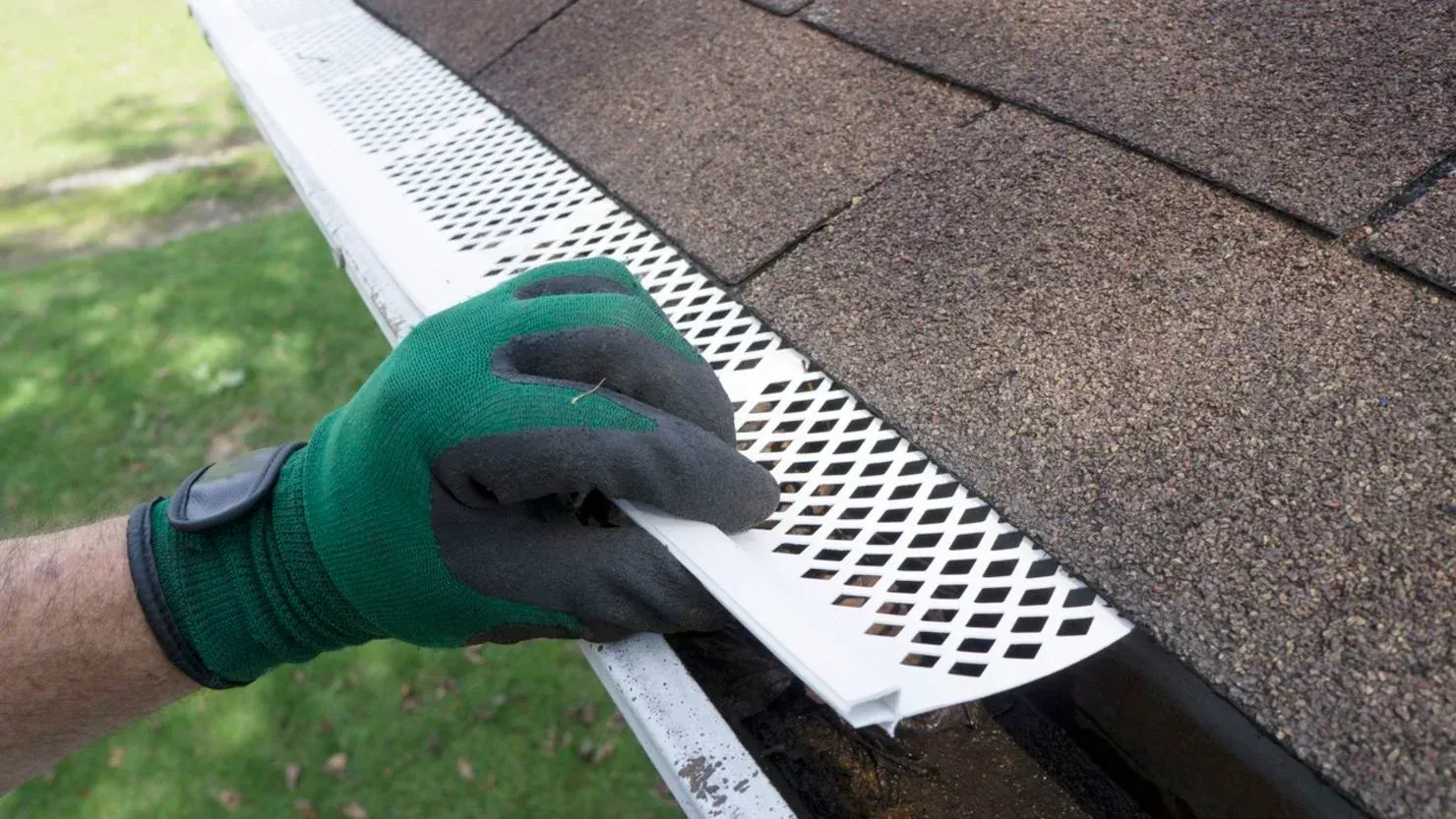 Gloved hand installing white gutter guard along roof edge