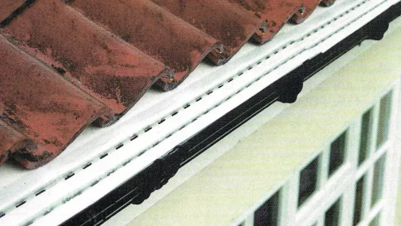 Rain gutter along red roof edge above a white-framed window