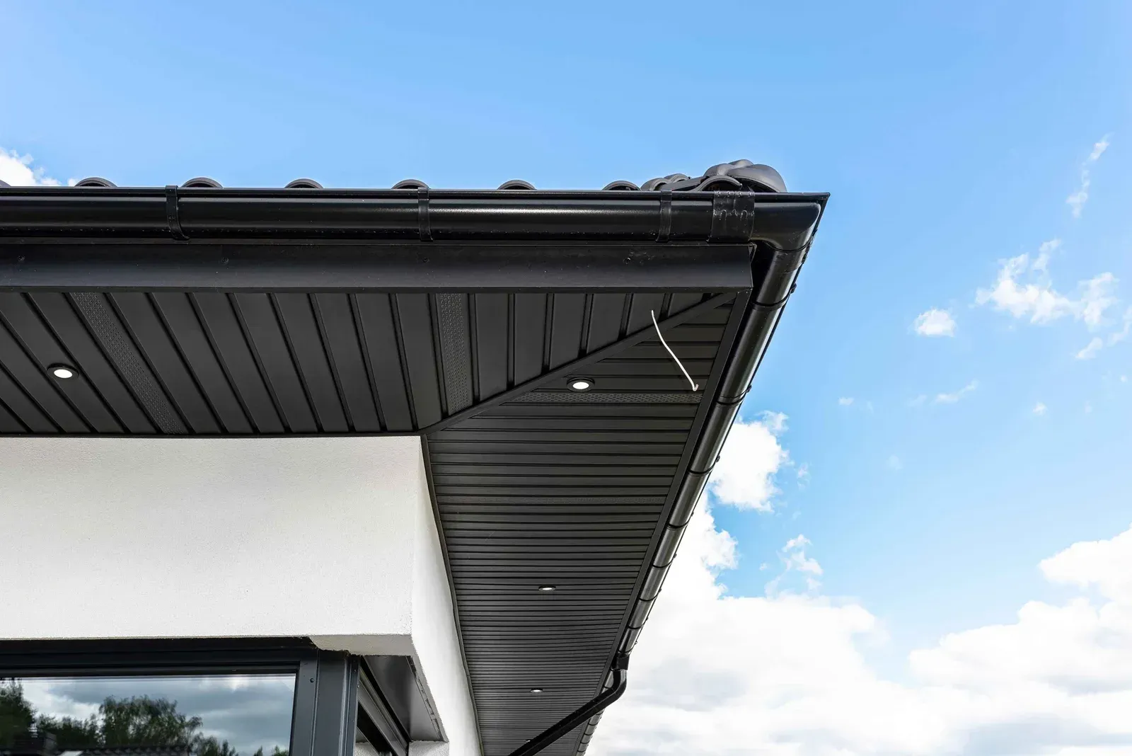 Modern house roof eaves with dark soffit and gutters against a bright blue sky