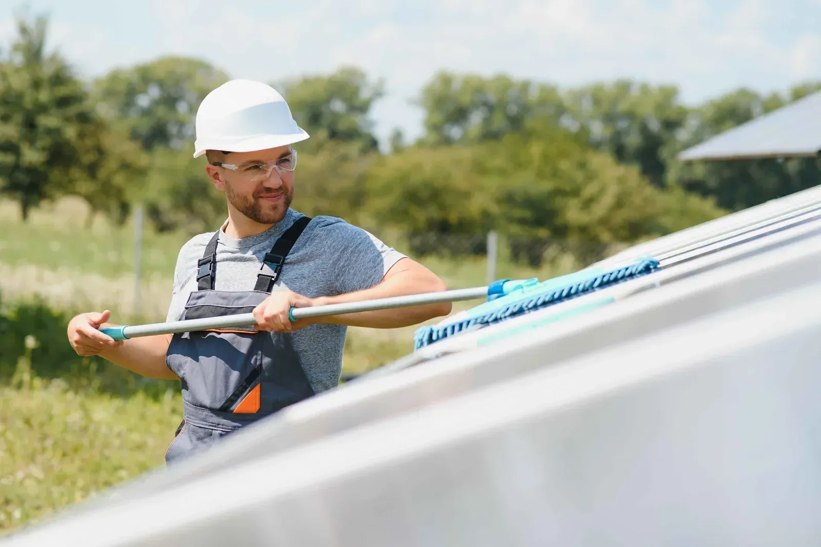 Worker in a white hard hat adjusts a solar panel with a tool in a grassy field.