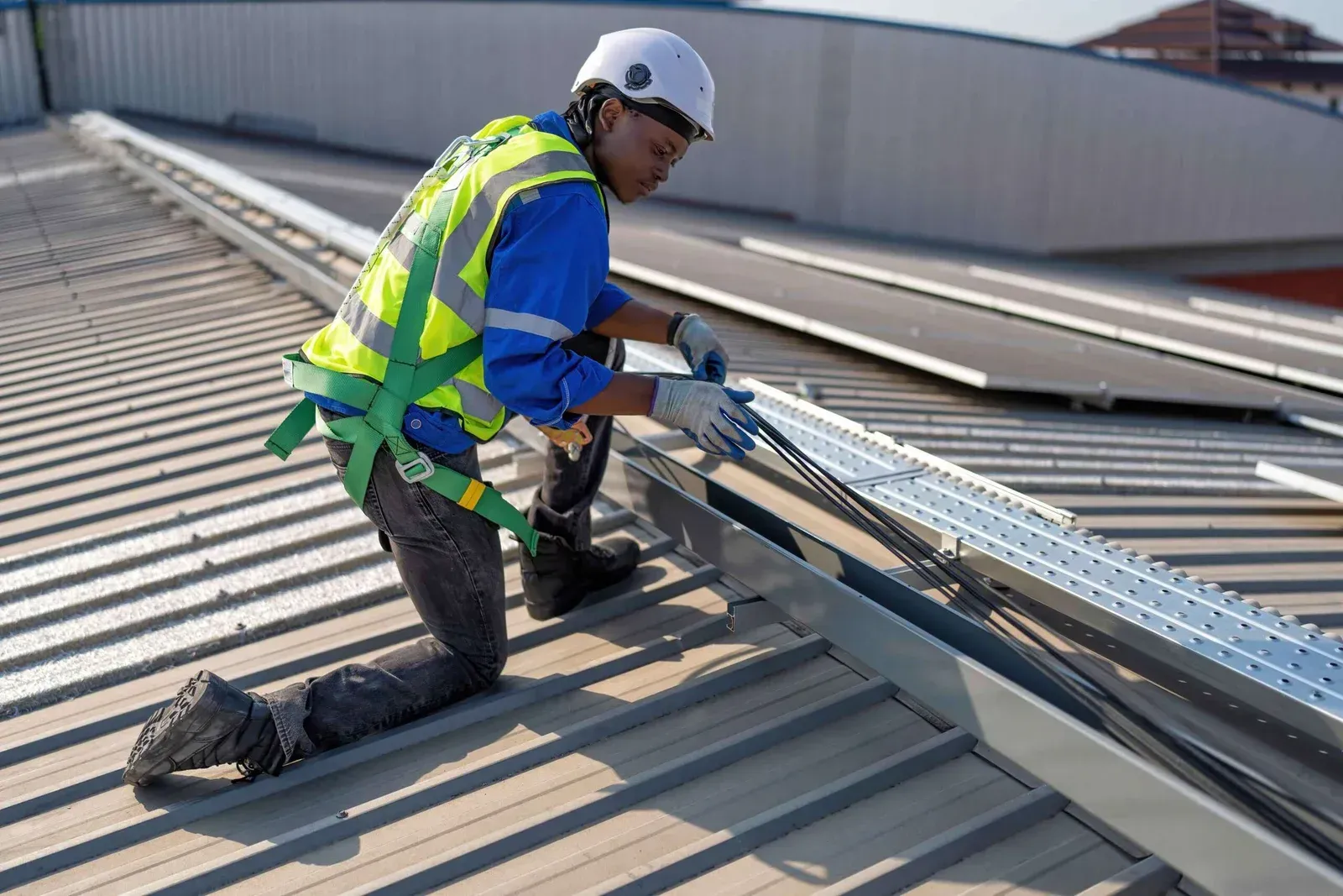Worker kneeling on a metal roof, installing or repairing roofing near a skylight, wearing safety gear