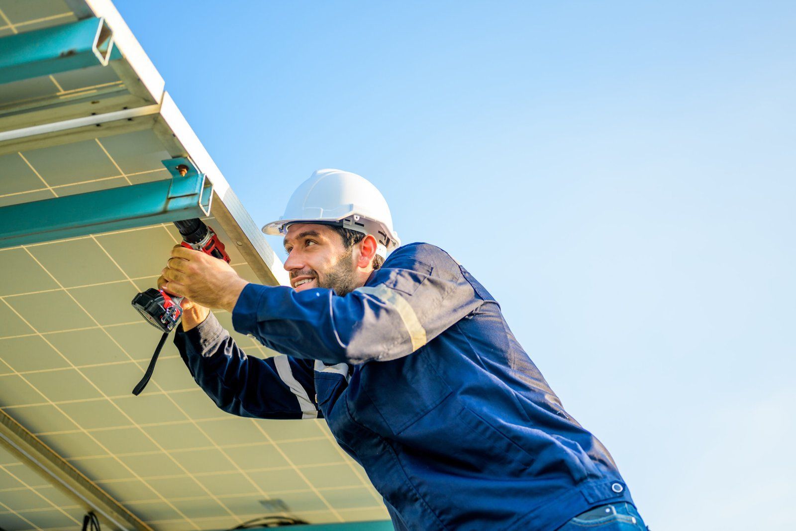 Worker in blue uniform and hard hat installing solar panels outdoors