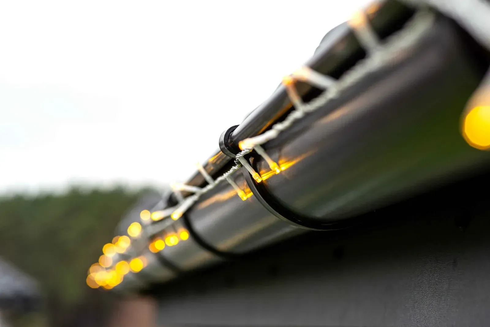 String lights glowing along a metal railing at dusk, with a blurred outdoor background