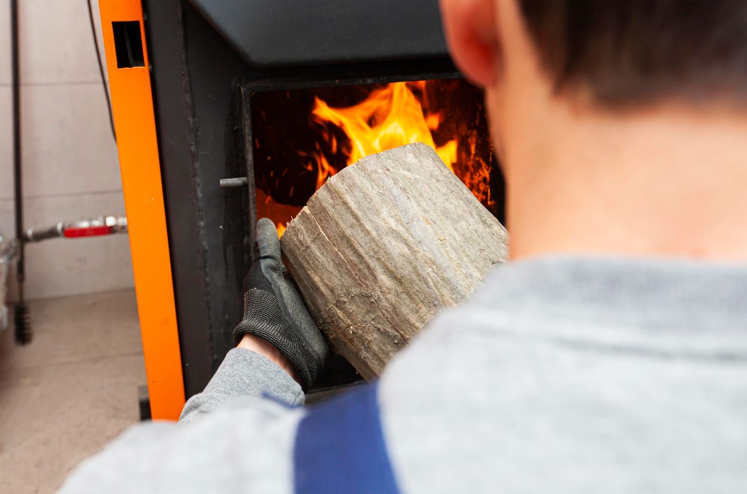 Person wearing a glove feeds a log into a lit wood stove.